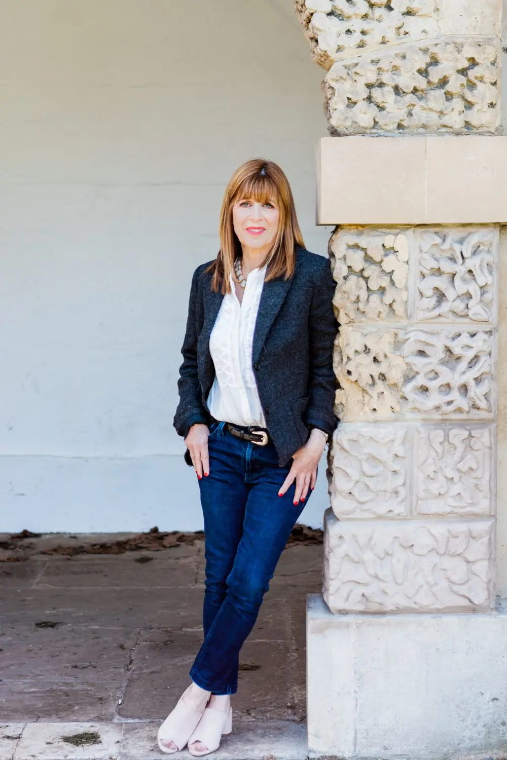 Dr Annie Kaszina standing calmly beside a carved stone pillar, warm and composed in a dark jacket and white blouse