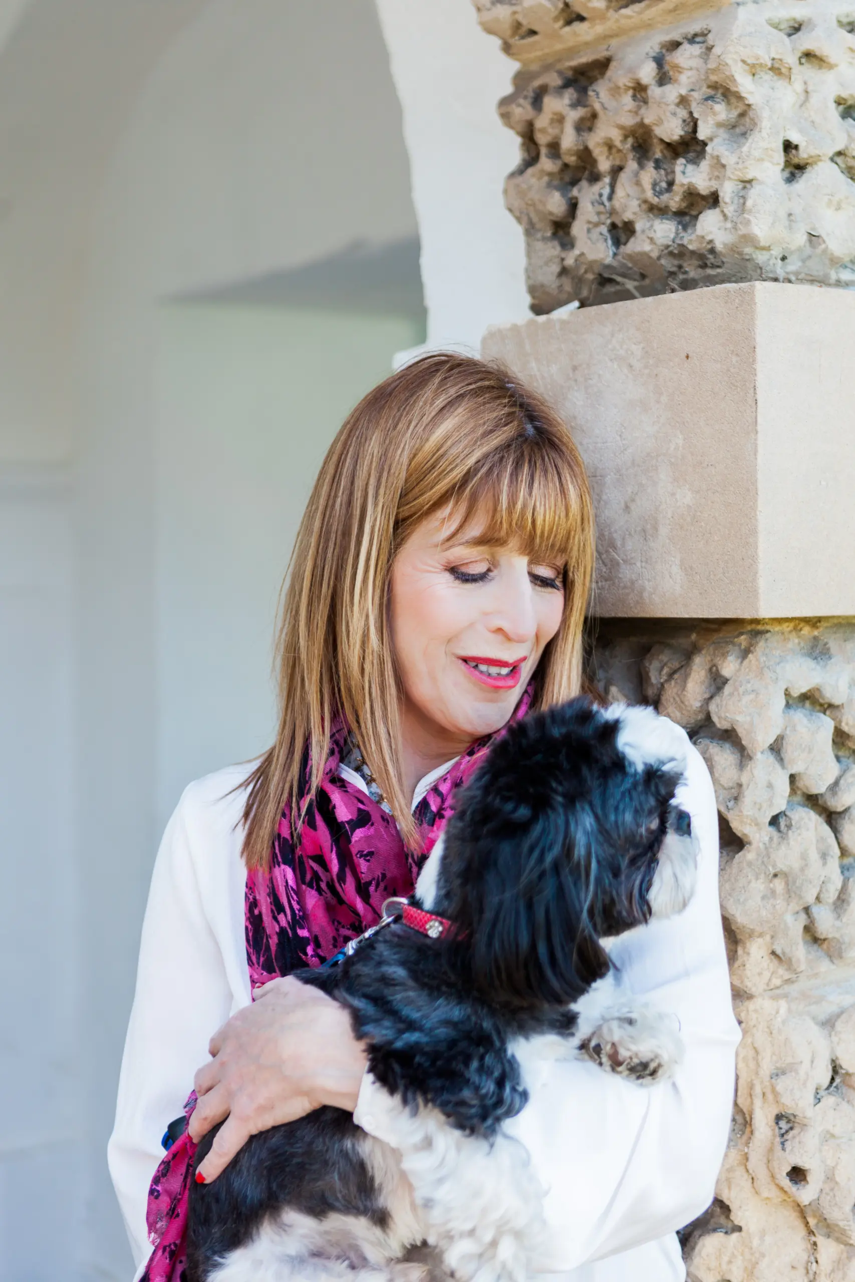 Dr Annie Kaszina holding her small dog tenderly beside a carved stone pillar