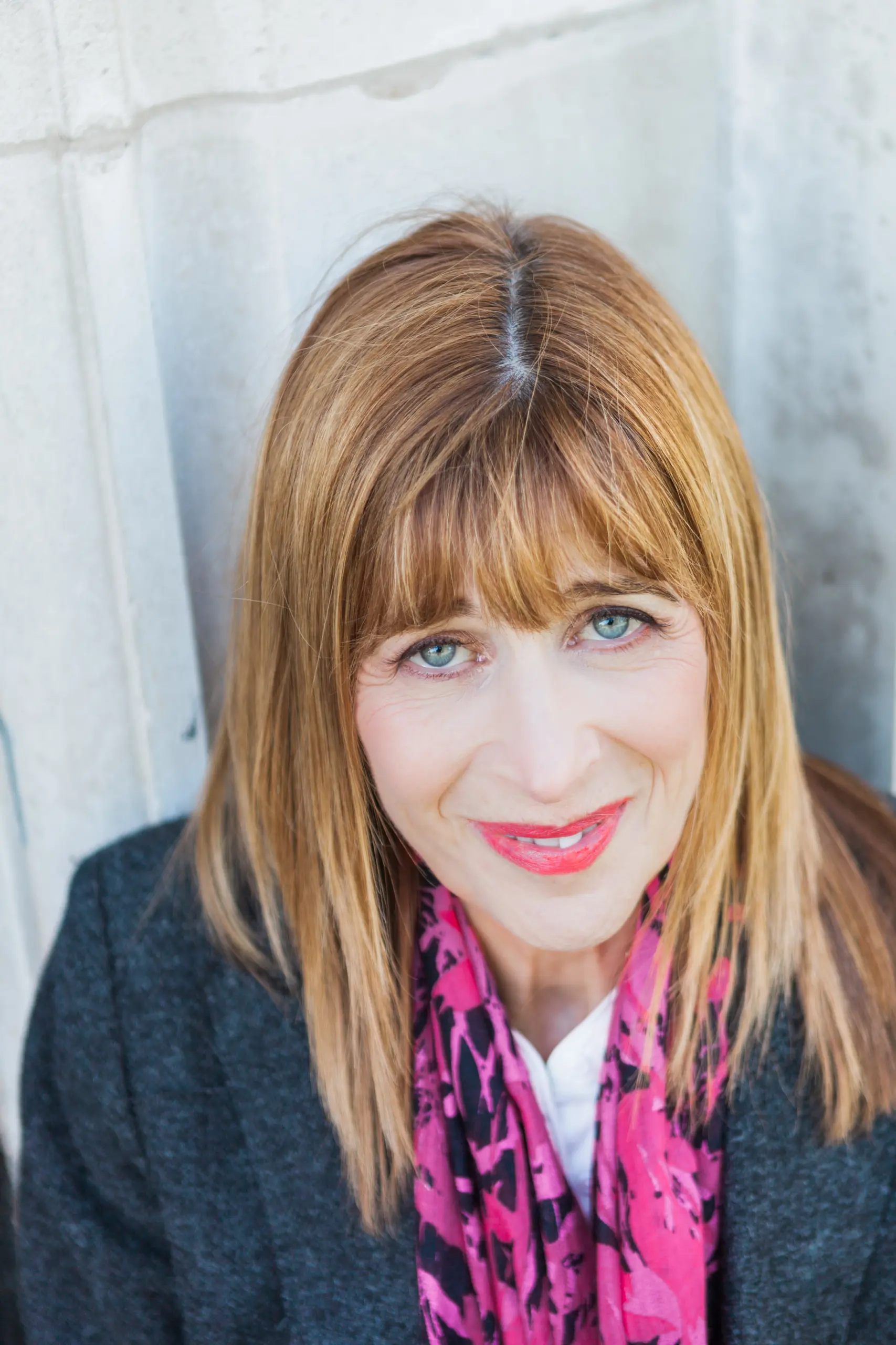 Dr Annie Kaszina smiling warmly at the camera in a grey jacket and pink patterned scarf