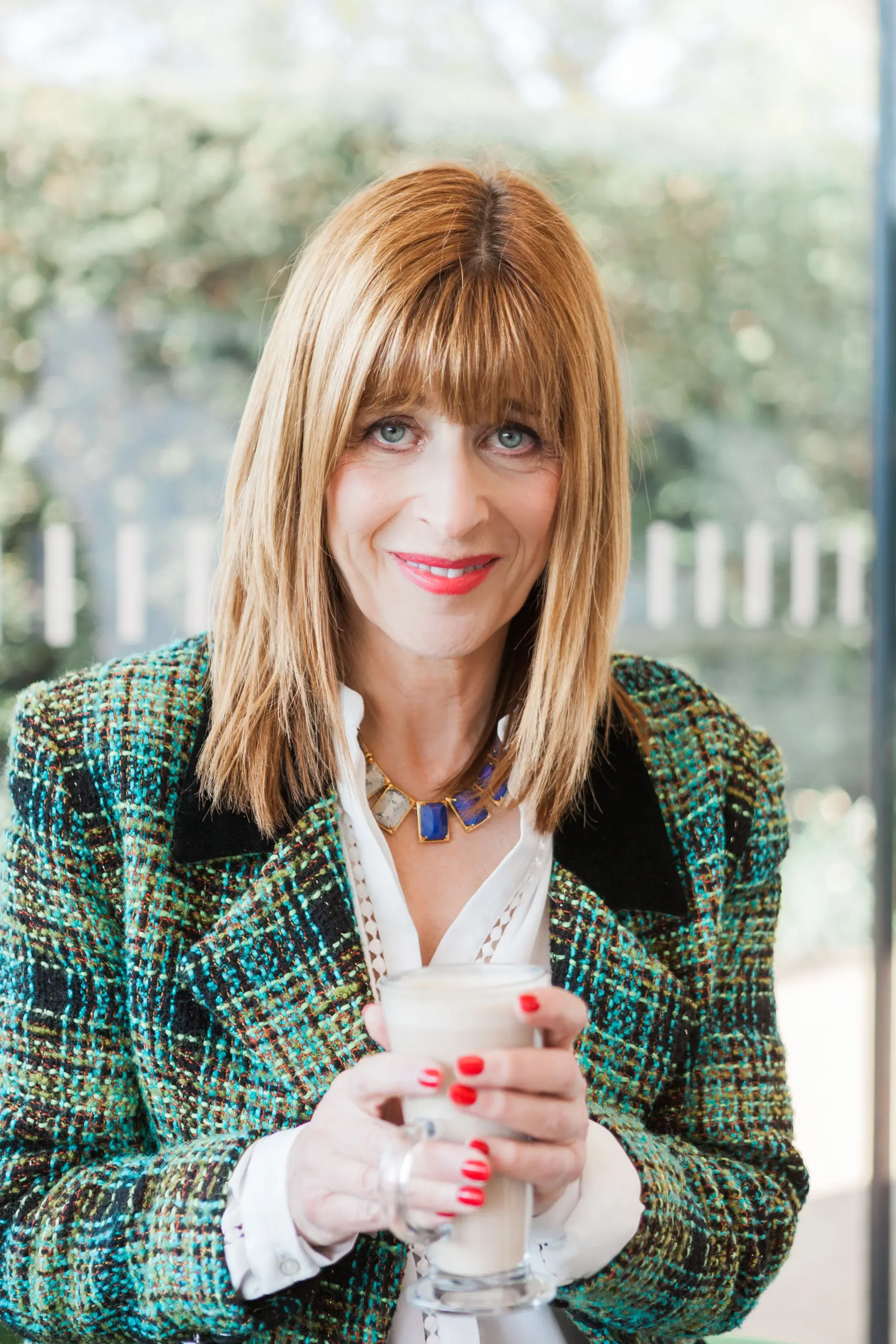 Dr Annie Kaszina in a green tweed jacket holding a cup, looking thoughtfully at the camera in a bright room